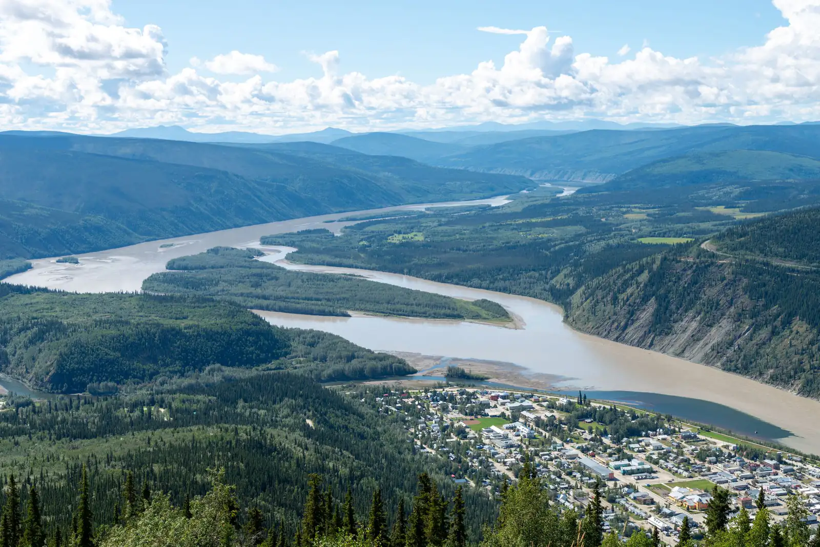 Aerial view of Dawson City beside the wide Yukon River surrounded by forested hills